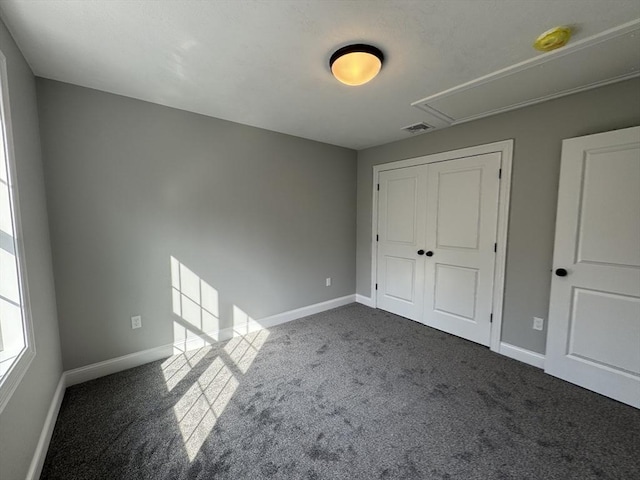 unfurnished bedroom with visible vents, baseboards, a closet, dark colored carpet, and attic access