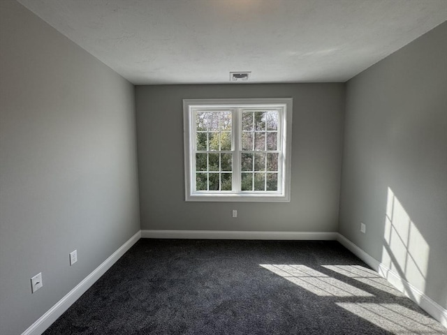 empty room with baseboards, visible vents, and dark carpet