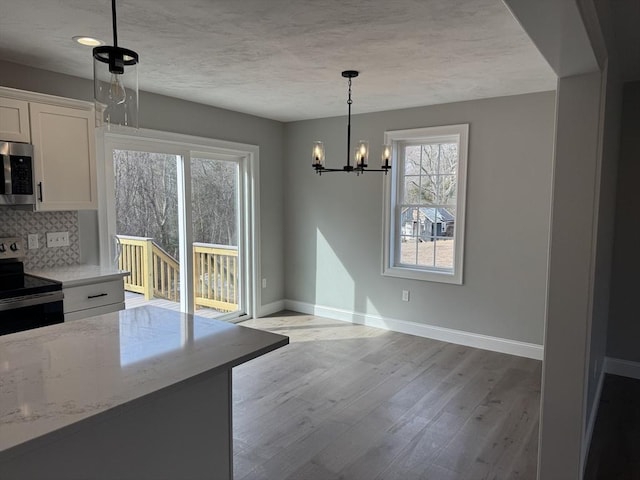 unfurnished dining area with light wood finished floors, baseboards, a textured ceiling, and an inviting chandelier