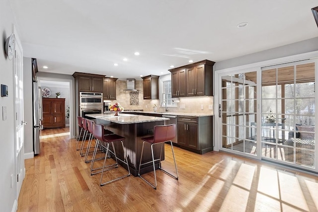 kitchen with a center island, wall chimney range hood, stainless steel appliances, decorative backsplash, and a breakfast bar area