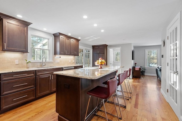 kitchen featuring decorative backsplash, light wood-type flooring, a kitchen island, a breakfast bar, and sink