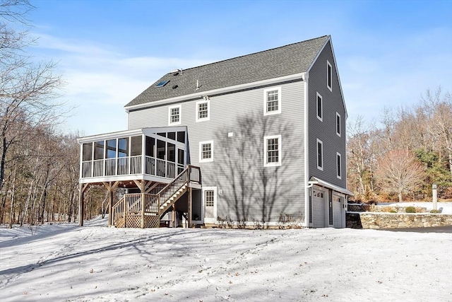 snow covered property with a garage and a sunroom