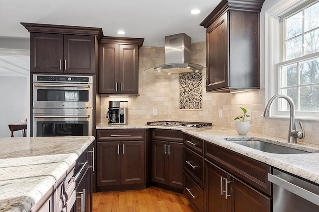 kitchen with tasteful backsplash, sink, light stone countertops, stainless steel appliances, and wall chimney exhaust hood