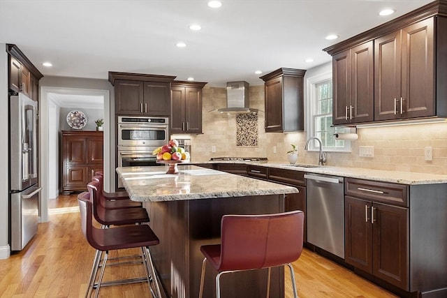 kitchen with wall chimney range hood, a kitchen island, light hardwood / wood-style flooring, a breakfast bar area, and stainless steel appliances