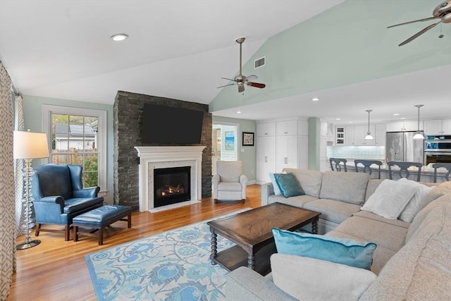 living room with light wood-style floors, a ceiling fan, visible vents, and vaulted ceiling