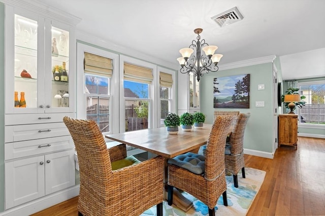 dining space with visible vents, baseboards, light wood finished floors, a chandelier, and ornamental molding