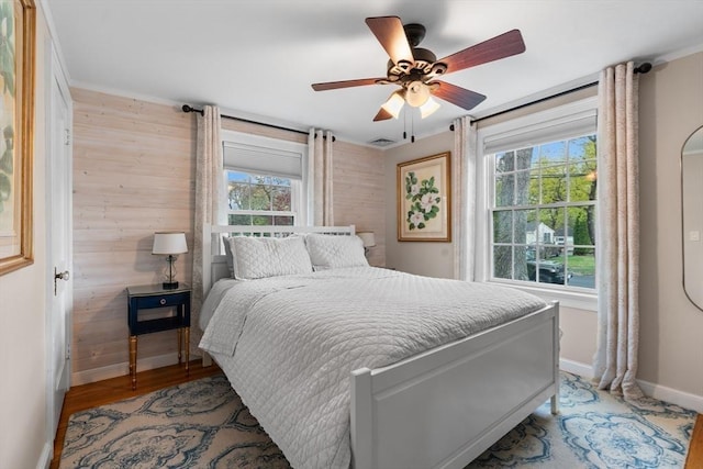 bedroom featuring visible vents, wood walls, wood finished floors, baseboards, and ceiling fan