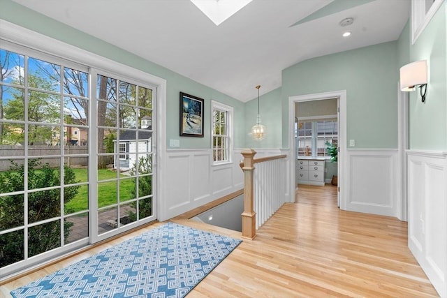 foyer entrance with light wood-type flooring, a decorative wall, vaulted ceiling with skylight, and a wainscoted wall