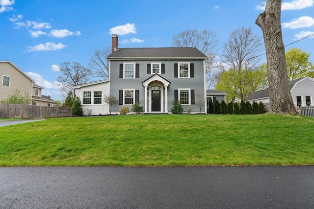colonial home with a front lawn, fence, and a chimney