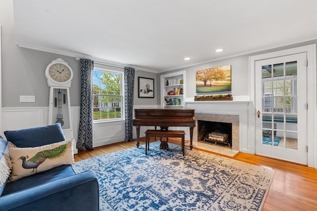 living area featuring crown molding, wood finished floors, a wainscoted wall, built in shelves, and a fireplace with flush hearth