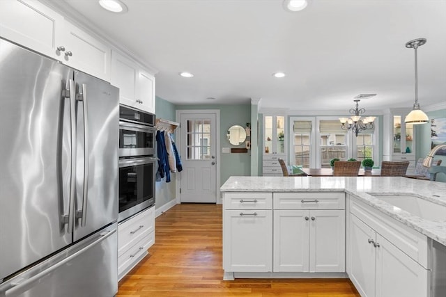 kitchen featuring white cabinets, a sink, a chandelier, stainless steel appliances, and light wood-type flooring