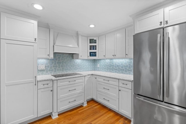 kitchen with black electric cooktop, stainless steel refrigerator, glass insert cabinets, custom range hood, and white cabinetry