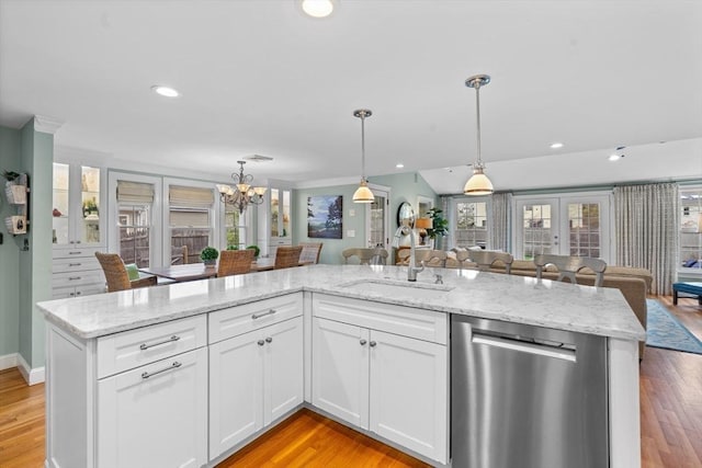 kitchen with a sink, white cabinetry, open floor plan, decorative light fixtures, and stainless steel dishwasher