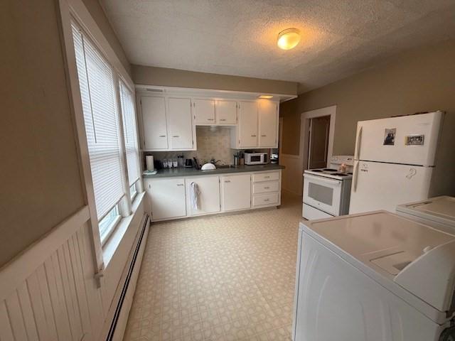 kitchen featuring washing machine and clothes dryer, white cabinets, white appliances, and baseboard heating