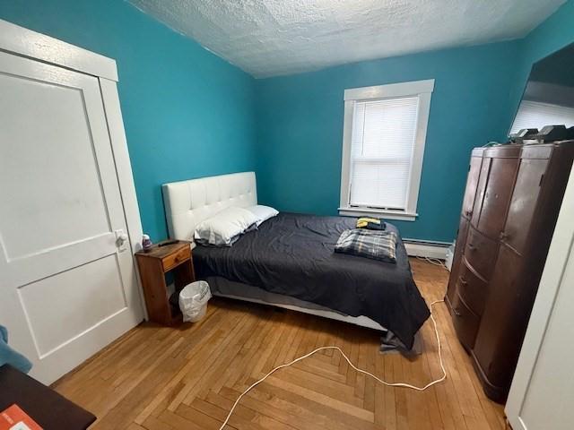 bedroom featuring a baseboard radiator, a textured ceiling, and light hardwood / wood-style flooring