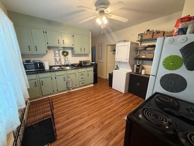 kitchen with stacked washer and dryer, light hardwood / wood-style flooring, ceiling fan, green cabinets, and electric range