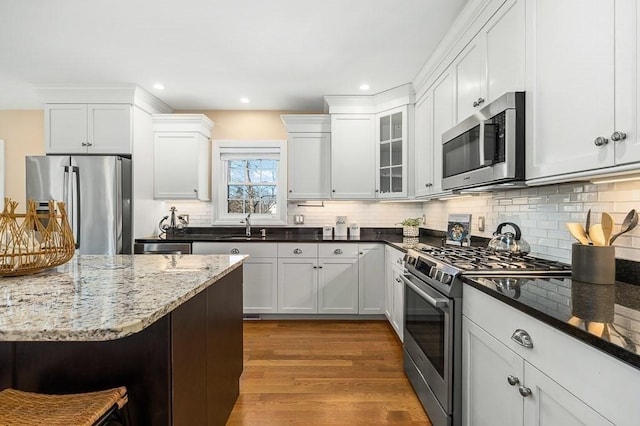 kitchen featuring a kitchen bar, wood-type flooring, appliances with stainless steel finishes, dark stone counters, and white cabinets