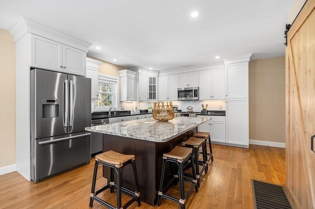 kitchen with a breakfast bar, white cabinetry, a center island, stainless steel appliances, and a barn door