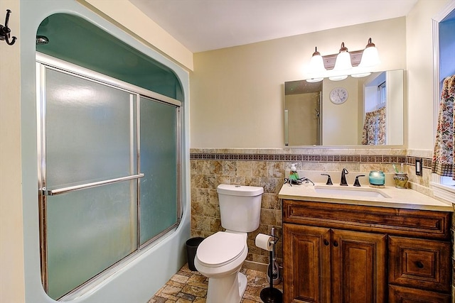 full bathroom featuring toilet, vanity, tile walls, and combined bath / shower with glass door