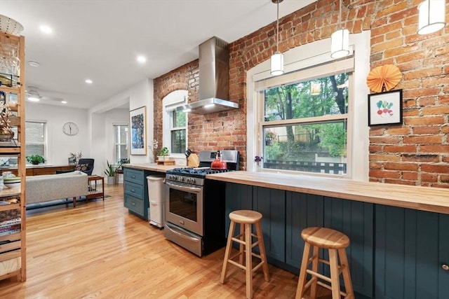 kitchen featuring stainless steel gas range oven, wall chimney exhaust hood, butcher block countertops, light wood finished floors, and brick wall