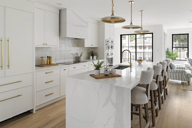 361 Walden Unit 361, Cambridge, MA 02138 - kitchen with custom range hood, light wood-style floors, decorative backsplash, black electric cooktop, and a kitchen bar