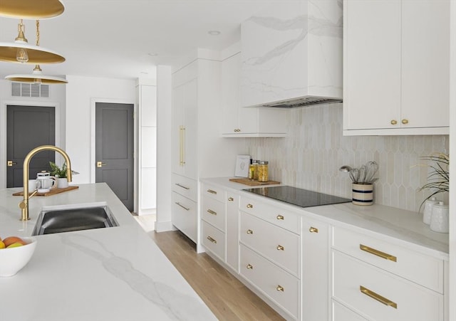 361 Walden Unit 361, Cambridge, MA 02138 - kitchen featuring black electric cooktop, custom range hood, backsplash, light wood-style flooring, and white cabinetry