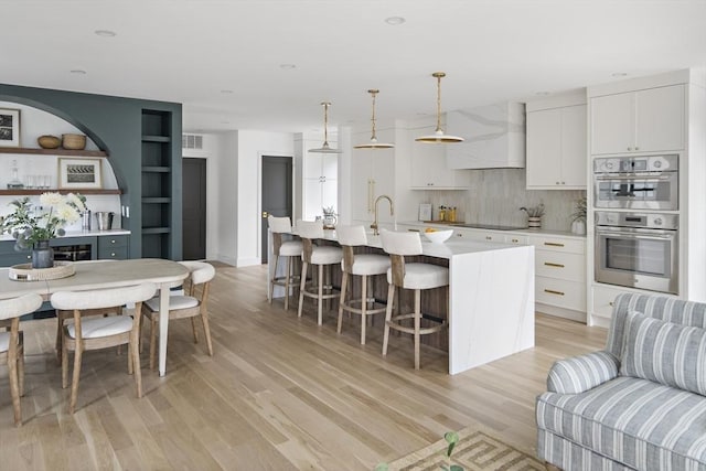 361 Walden Unit 361, Cambridge, MA 02138 - kitchen with premium range hood, light wood-style floors, stainless steel double oven, backsplash, and white cabinets