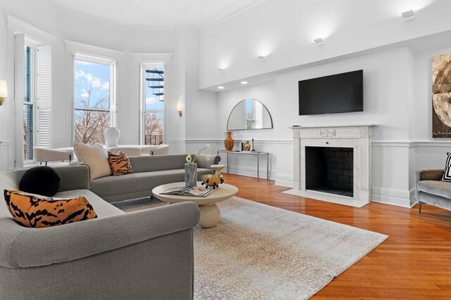 living area featuring a fireplace with flush hearth, wood finished floors, and crown molding