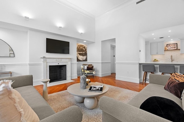 living room with a fireplace with flush hearth, wood finished floors, crown molding, baseboards, and a towering ceiling