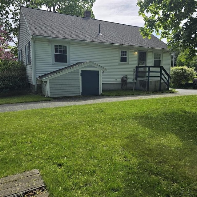 back of property featuring a chimney, a shingled roof, and a yard