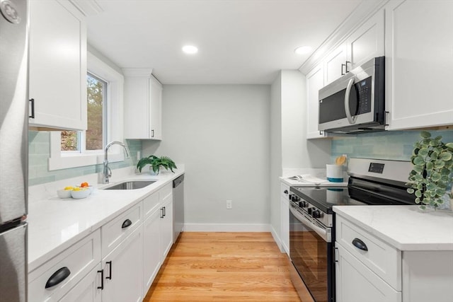 kitchen with backsplash, baseboards, light wood-type flooring, stainless steel appliances, and a sink