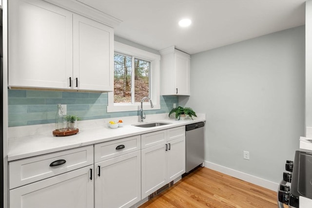 kitchen with a sink, backsplash, baseboards, light wood-type flooring, and stainless steel dishwasher