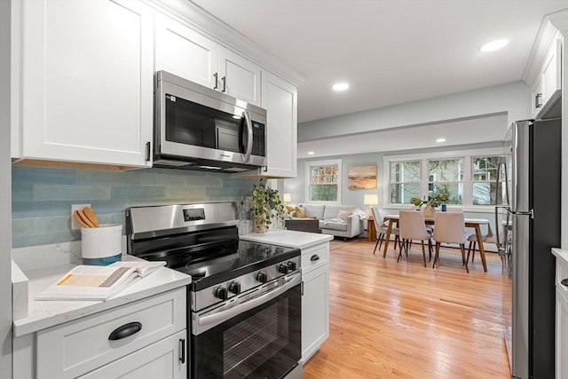 kitchen featuring light wood-type flooring, open floor plan, stainless steel appliances, white cabinets, and decorative backsplash