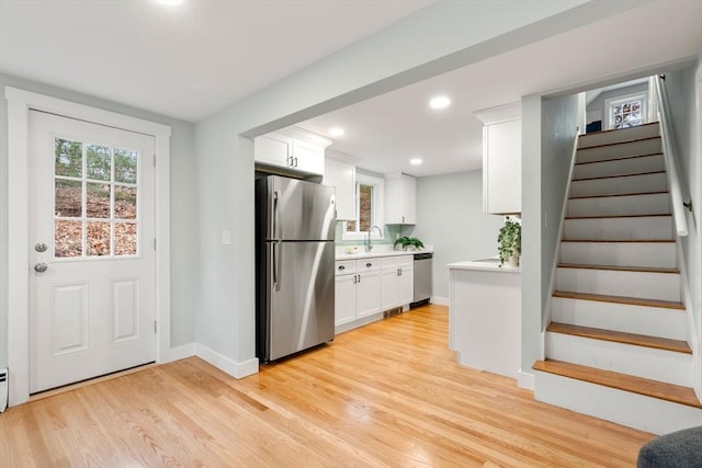 kitchen with light countertops, light wood-style flooring, appliances with stainless steel finishes, white cabinetry, and a sink