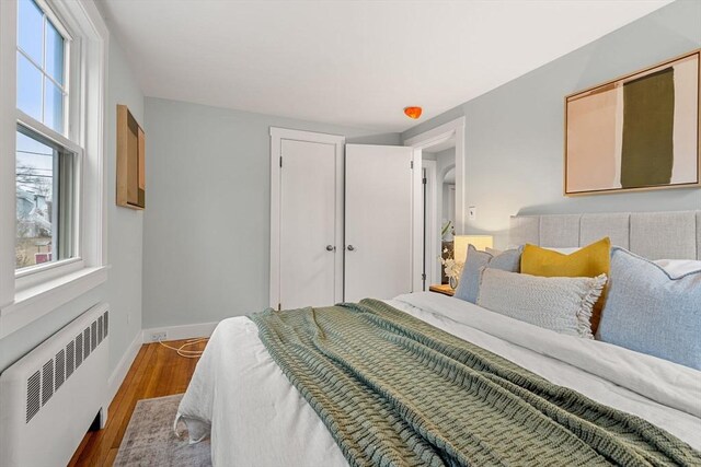 bedroom with dark wood finished floors, radiator heating unit, baseboards, and a closet