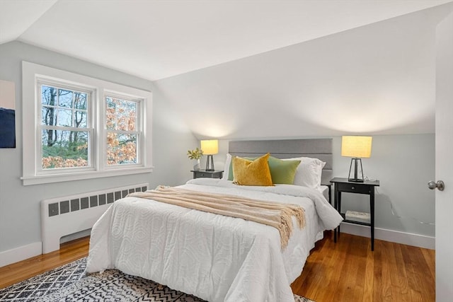 bedroom featuring lofted ceiling, radiator heating unit, wood finished floors, and baseboards