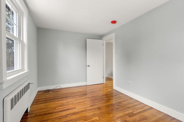 unfurnished room featuring radiator, baseboards, and wood finished floors