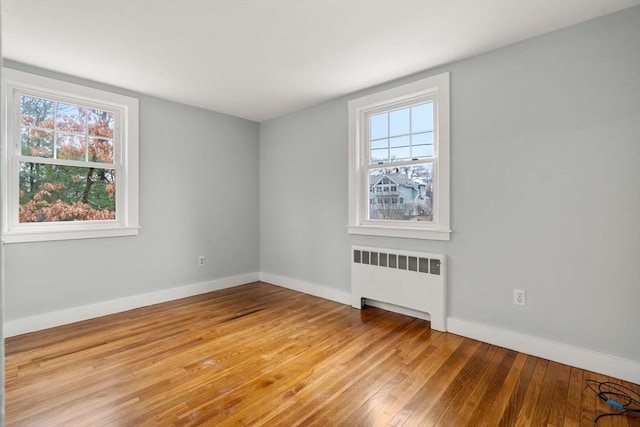 empty room with baseboards, radiator heating unit, and light wood-style floors