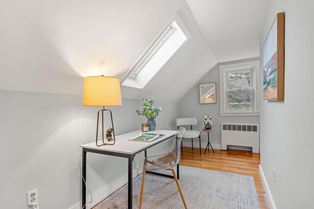 home office with vaulted ceiling with skylight, radiator heating unit, baseboards, and wood finished floors