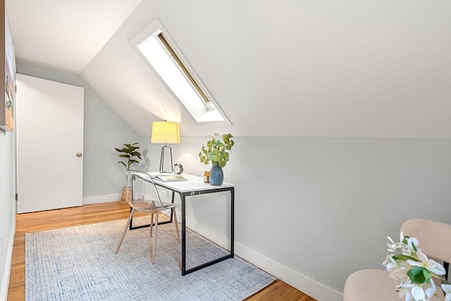 office area with light wood finished floors, vaulted ceiling with skylight, and baseboards