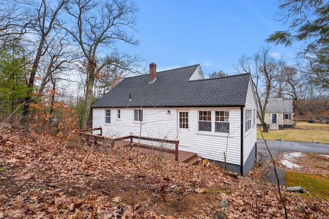 rear view of house featuring entry steps, a chimney, and a shingled roof