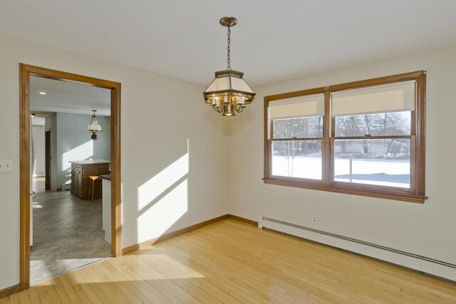 spare room with wood-type flooring, an inviting chandelier, and baseboard heating