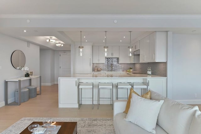 kitchen featuring pendant lighting, tasteful backsplash, white cabinets, a kitchen breakfast bar, and crown molding