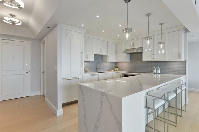 kitchen featuring sink, light stone counters, hanging light fixtures, white cabinets, and backsplash