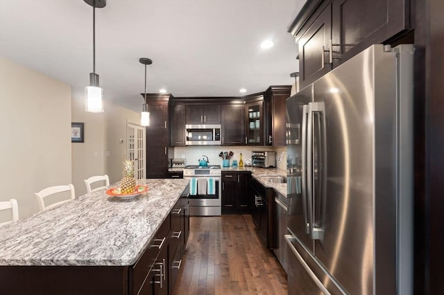 11 Winslow Way, Swansea, MA 02777 - kitchen featuring appliances with stainless steel finishes, tasteful backsplash, dark brown cabinetry, a center island, and light stone counters
