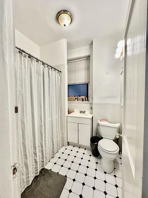 bathroom with tile patterned floors, toilet, vanity, wainscoting, and tile walls
