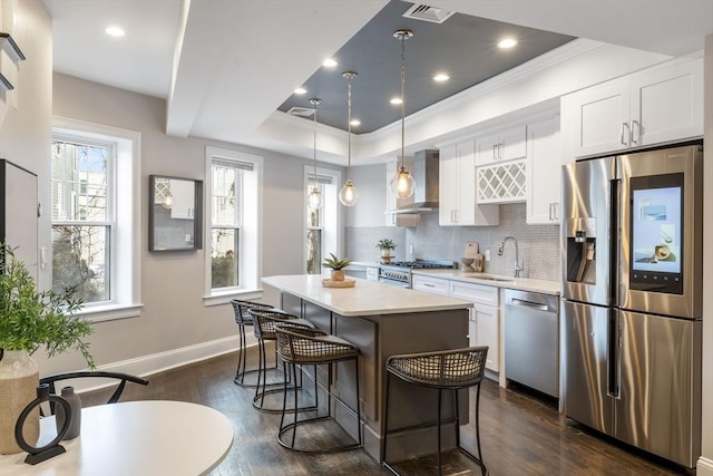 kitchen with a center island, sink, stainless steel appliances, wall chimney range hood, and white cabinets