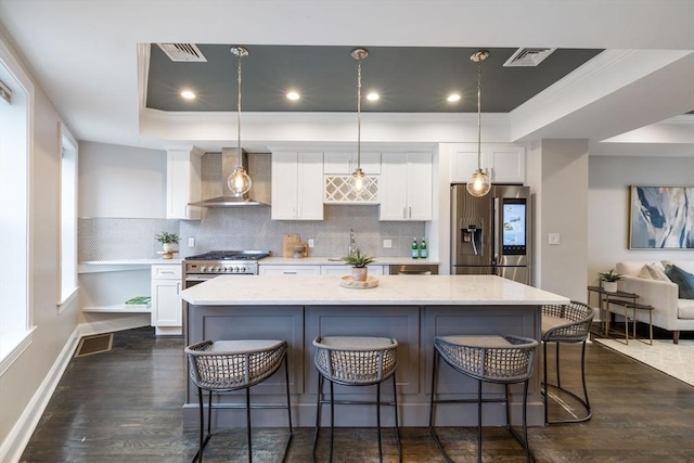 kitchen featuring wall chimney exhaust hood, decorative light fixtures, white cabinetry, and appliances with stainless steel finishes