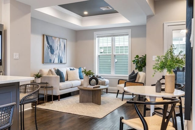 living room featuring dark hardwood / wood-style floors, a raised ceiling, and crown molding