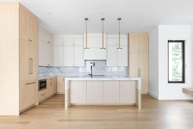 1597 Centre St Unit A, Newton, MA 02461 - kitchen featuring light brown cabinetry, a center island with sink, light countertops, light wood finished floors, and tasteful backsplash